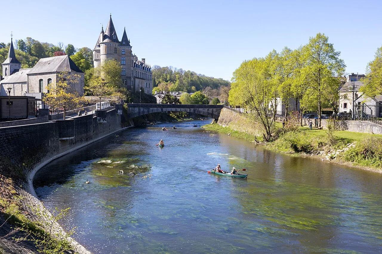 Kayakkers op de Ourthe rivier met het kasteel van Durbuy op de achtergrond onder een stralend blauwe hemel