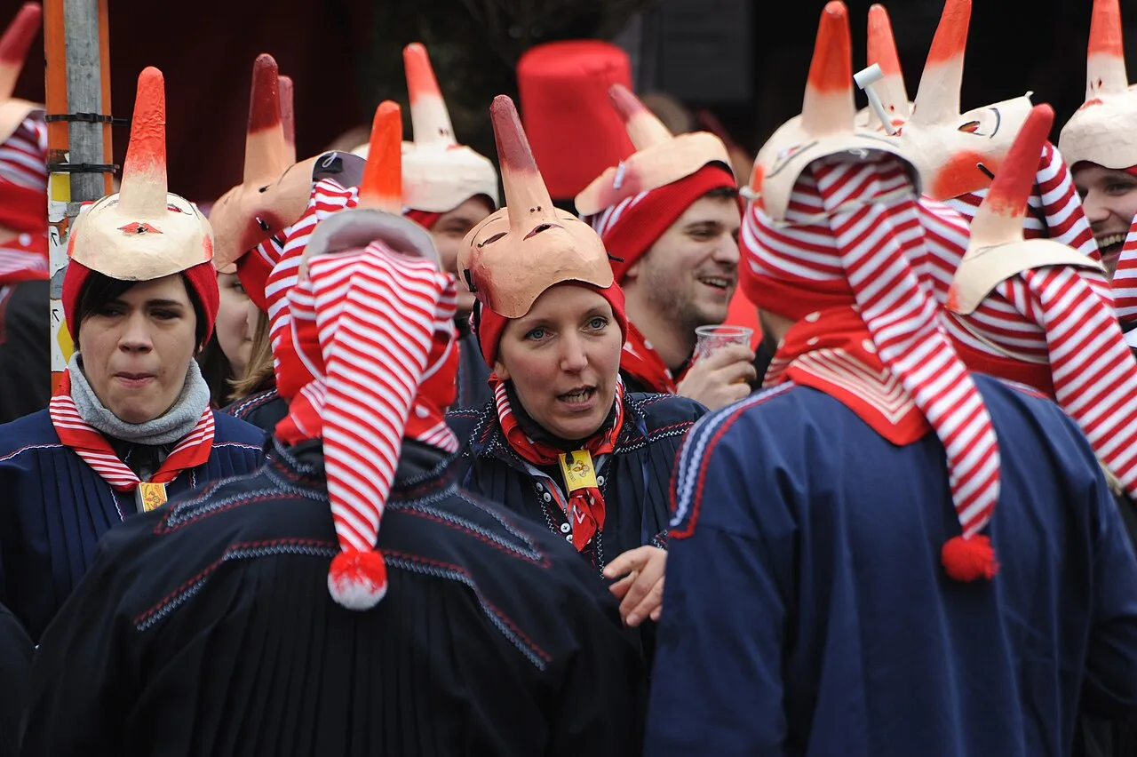 Deelnemers aan het Cwarmê carnaval van Malmedy in traditionele kostuums met kegelvormige hoeden in rood-wit gestreepte stof