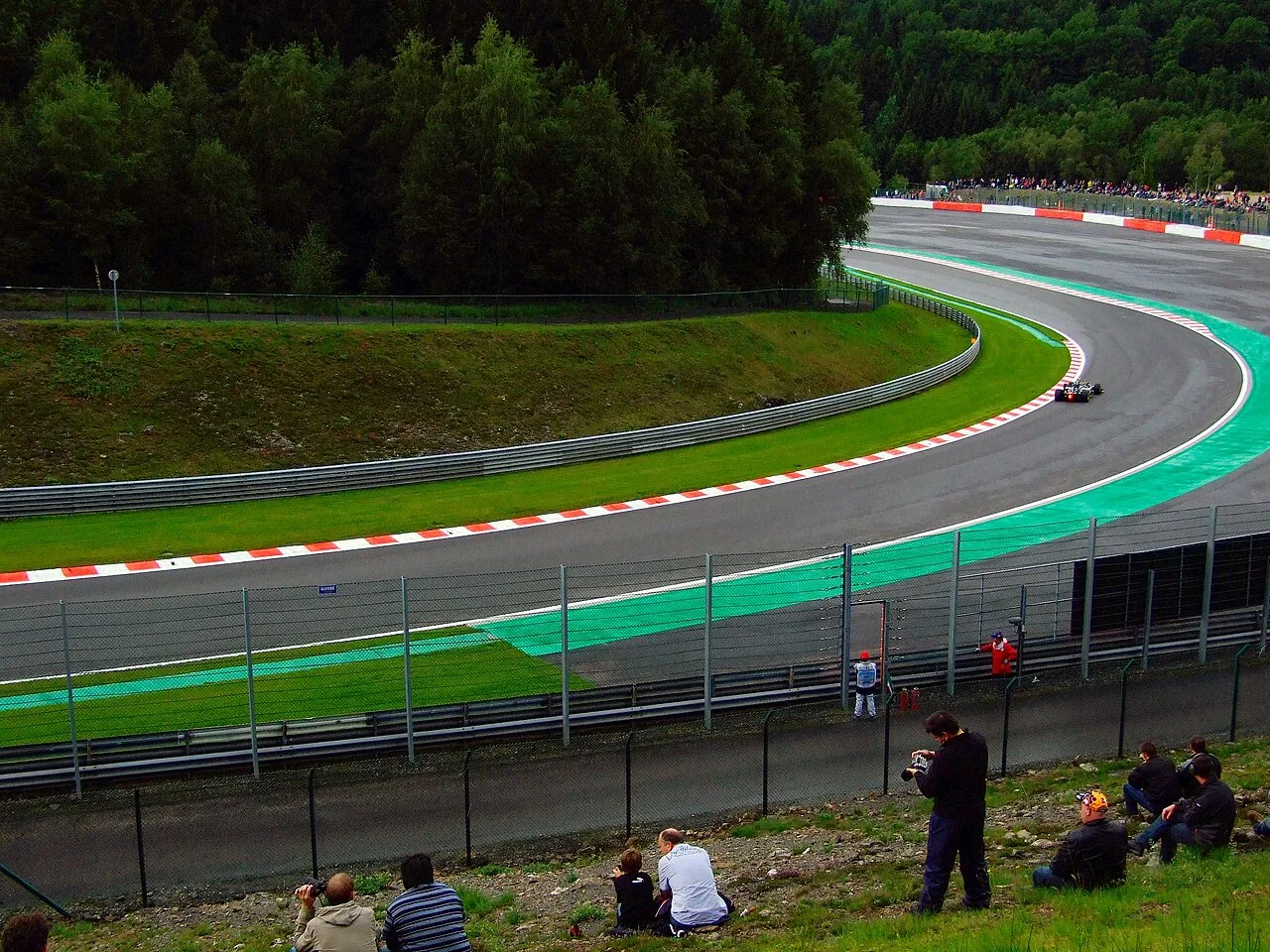 Toeschouwers zitten op een grasheuveltje langs het circuit van Spa-Francorchamps en kijken naar de raceauto's
