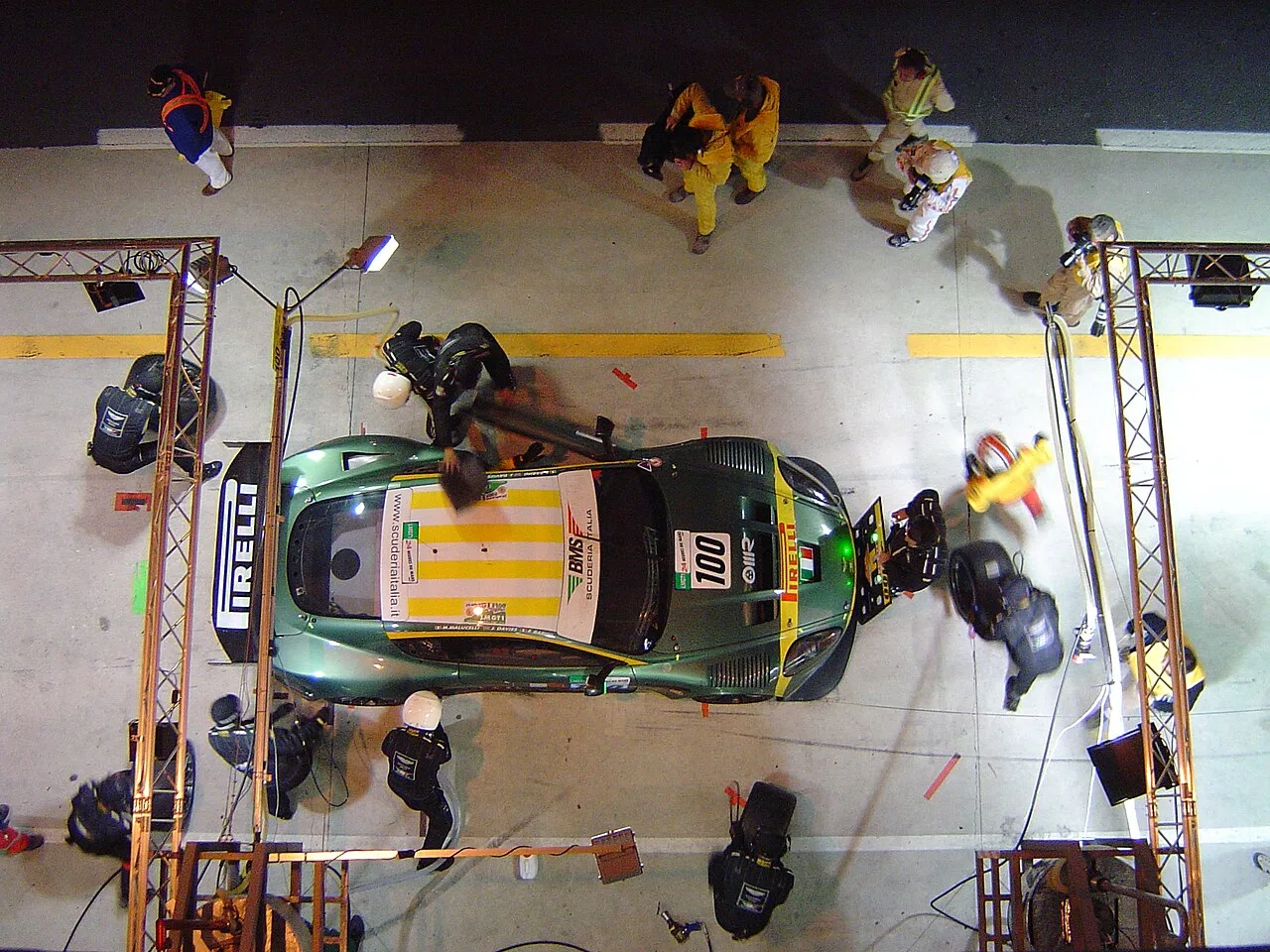 Nacht pitstop bij 24-uursrace: monteurs bedienen GT-racewagen van bovenaf in verlichte pitbox