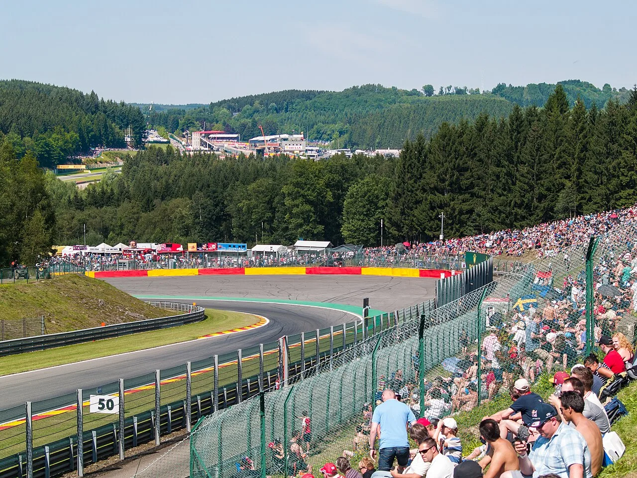 Pouhon-bocht op Spa-Francorchamps tijdens de Belgische Grand Prix, met vol publiek langs het circuit en Ardense bossen op de achtergrond
