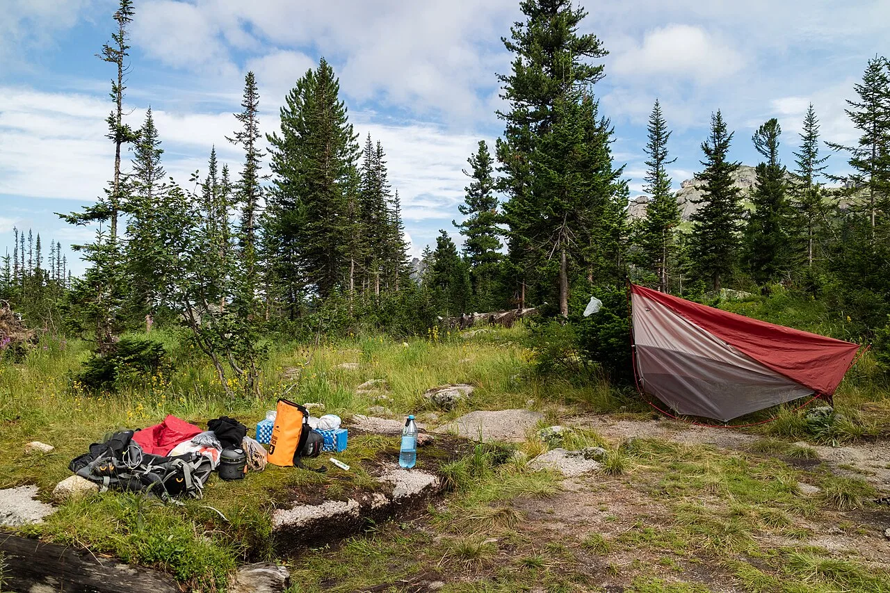 Kampeeruitrusting en rugzak uitgespreid bij een tent in een bosrijke omgeving, klaar voor een outdoor-weekend